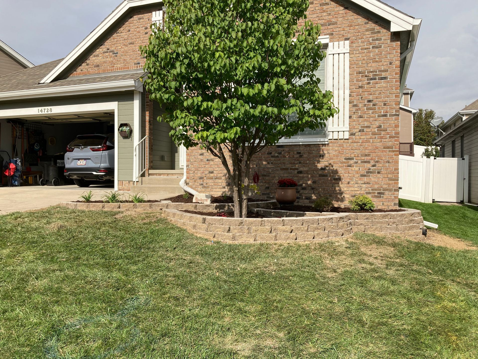 a brick house with a tree in front of it and a car parked in the garage