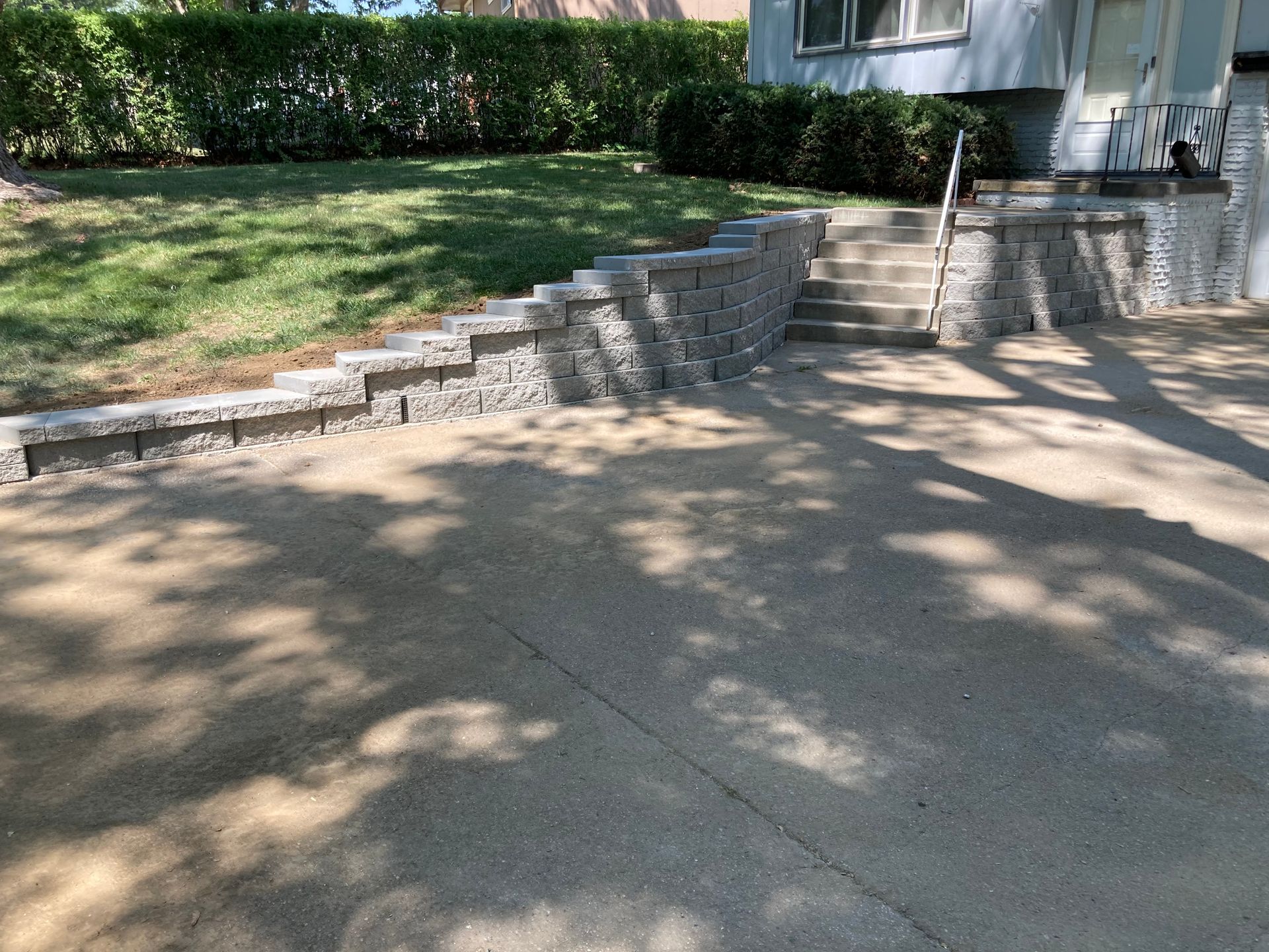 a driveway with a stone wall and stairs leading up to a house