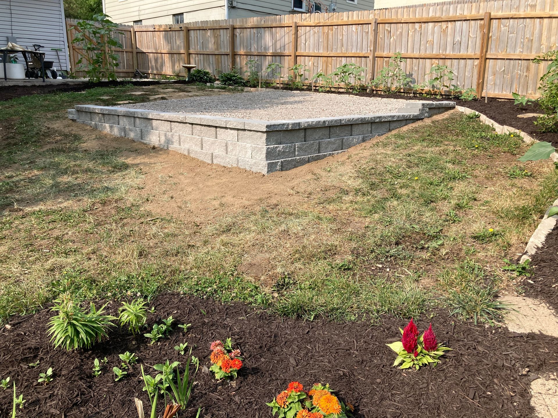 a backyard with a brick wall , flowers , and a wooden fence