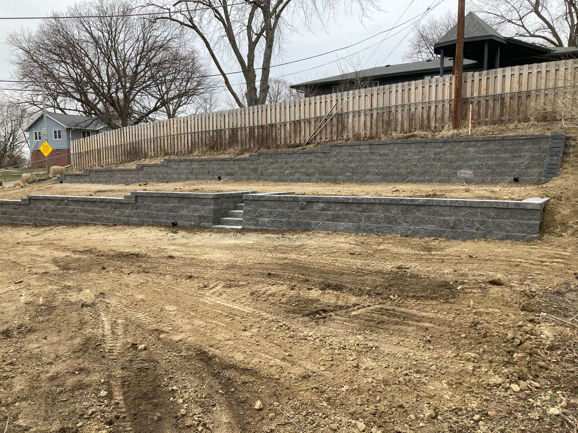 a brick wall is sitting on top of a dirt hill next to a house