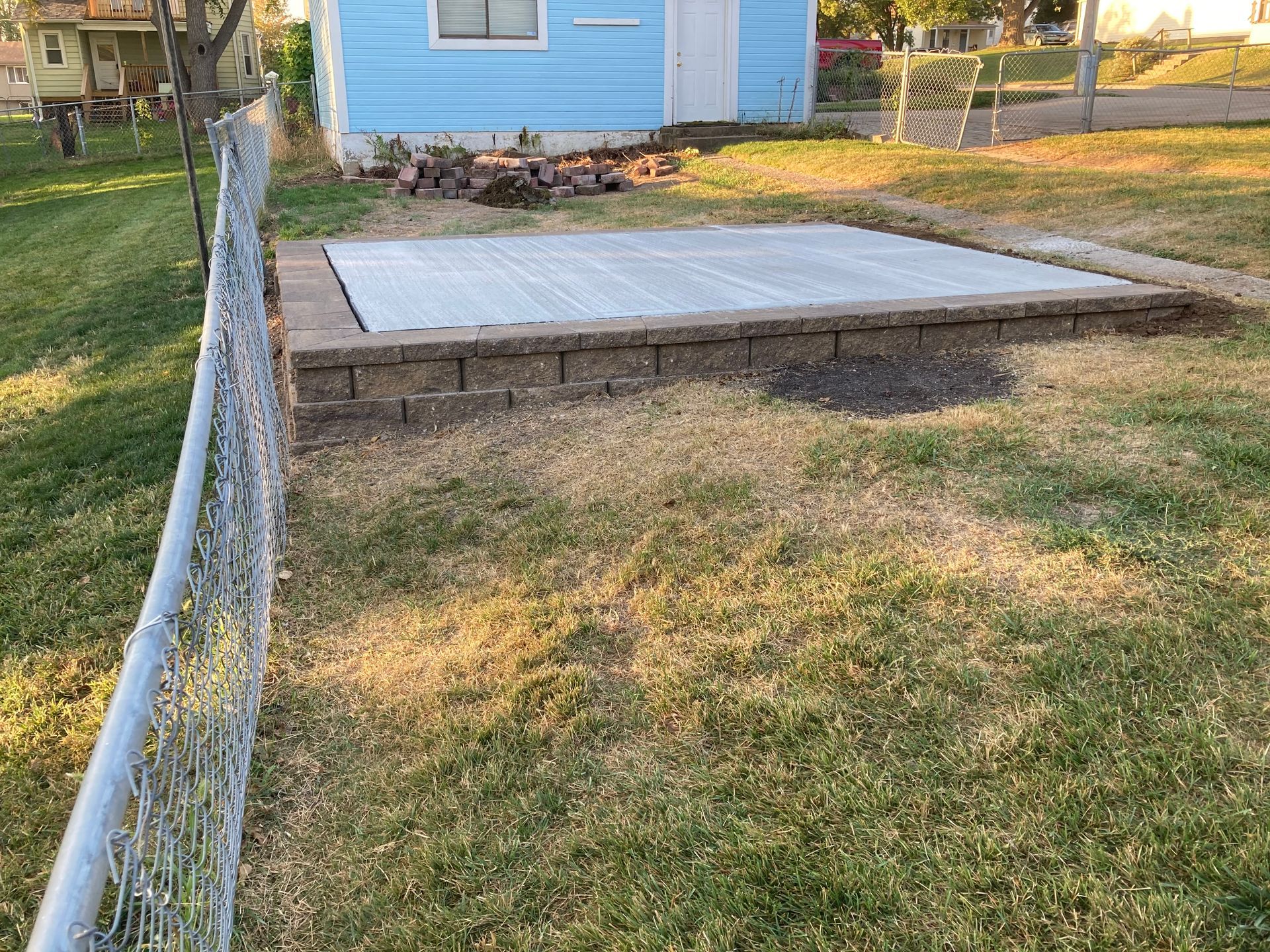 a blue house is behind a chain link fence with a concrete platform in front of it