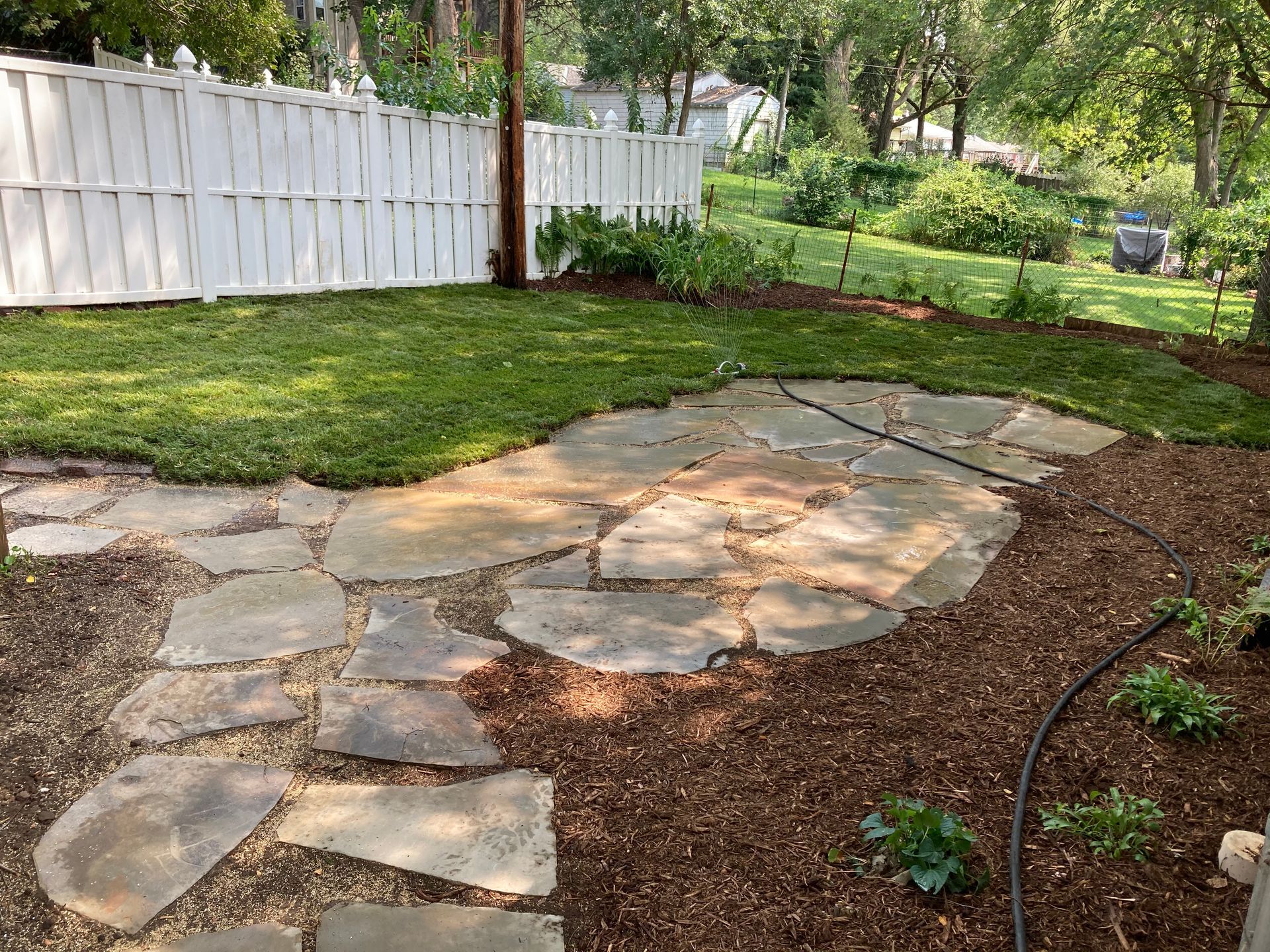 a backyard with a stone walkway and a white fence