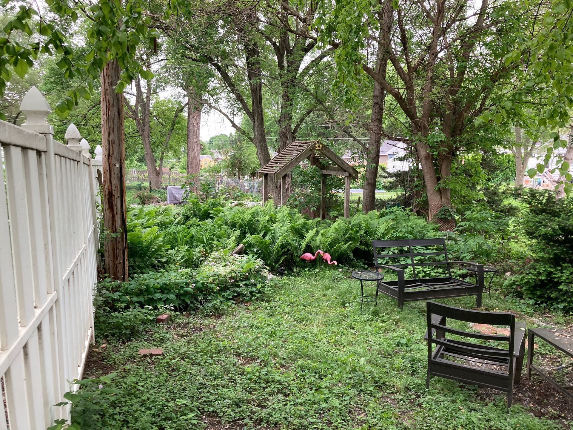 a backyard with a white fence, benches, and trees
