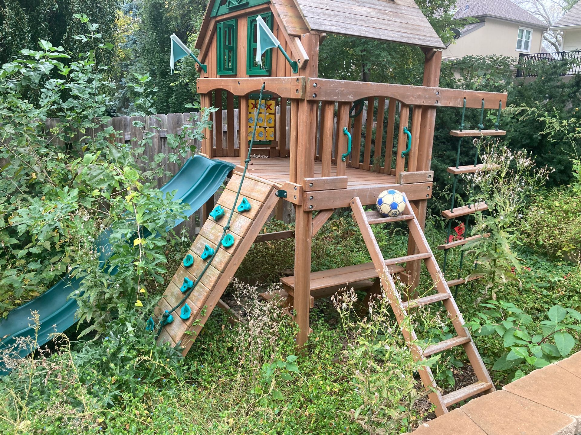 A wooden playground structure with a slide, climbing wall, and ladder set in a grassy backyard.