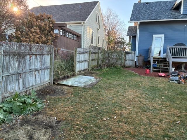 Backyard with weathered wooden fence, brown grass, and two-story houses.