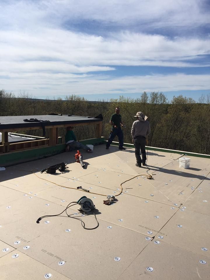 Three people working on a roof on a sunny day. Tools and materials are scattered on the surface.