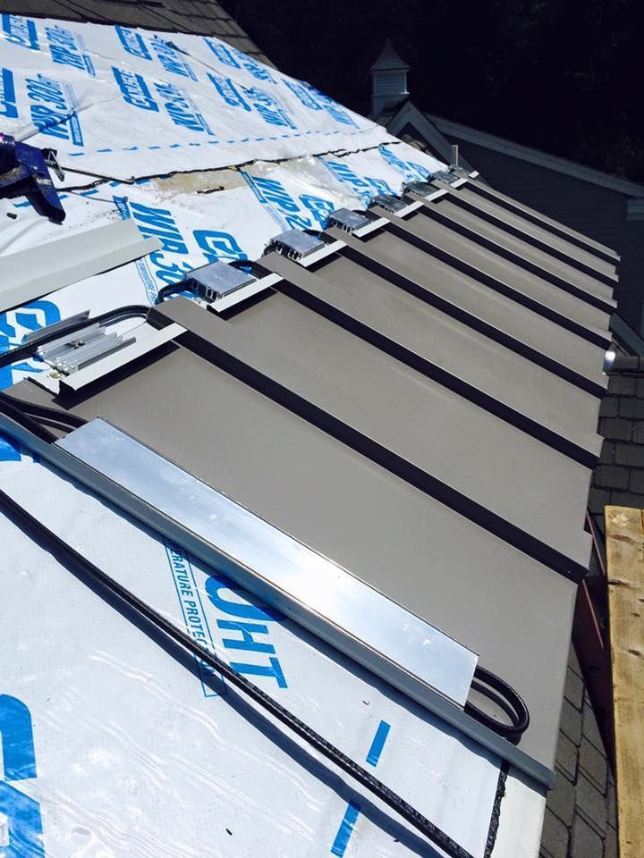 Gray metal roof being installed, with silver flashing and blue underlayment visible.