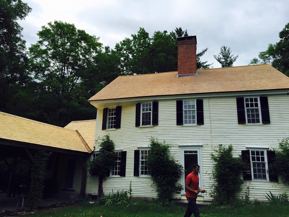 White, two-story house with black shutters, attached covered walkway, red brick chimney. Person walks in front of the house.