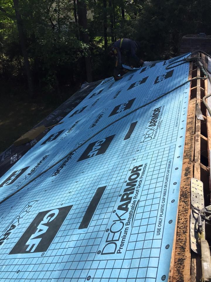 Roofing crew installing blue DeckArmor underlayment on a house roof.