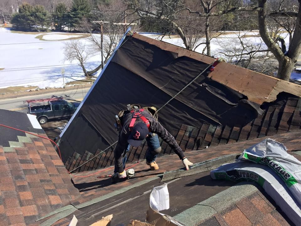 Roofer on a roof removing old shingles; a truck is in the background.