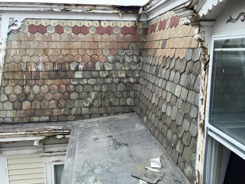 Exterior view of old building with weathered, hexagonal shingles and damaged trim.