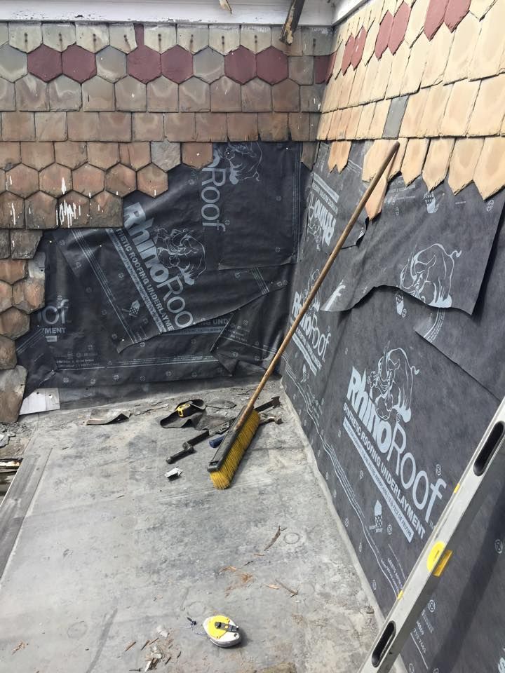 Roofing project with black underlayment, various roof tiles, and tools in a partially constructed area.