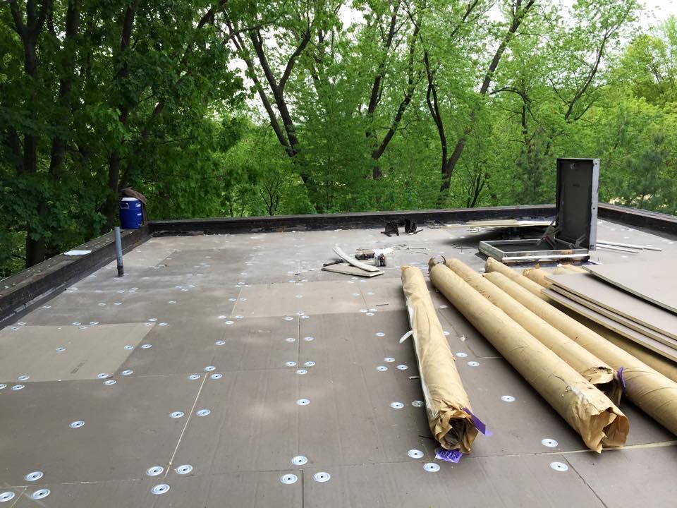 Flat roof with insulation panels, rolls of material, and a person standing, trees in the background.