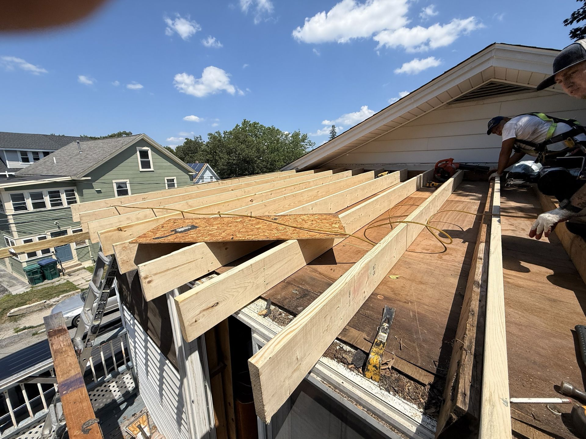 Roof construction: Wood beams and plywood on a house roof under a blue sky, workers installing.