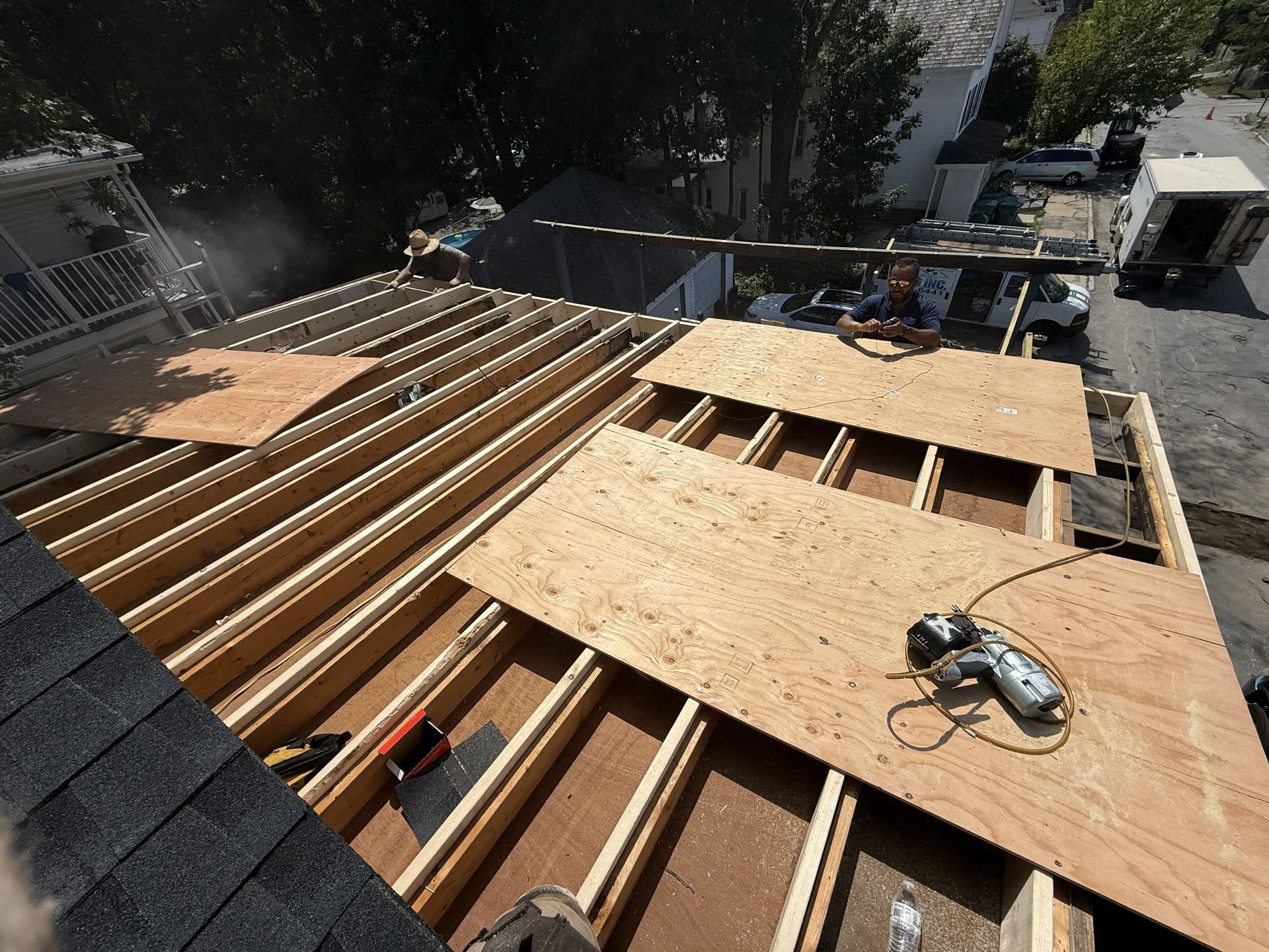 Roof under construction; plywood sheets laid on wooden beams; worker and tools visible.