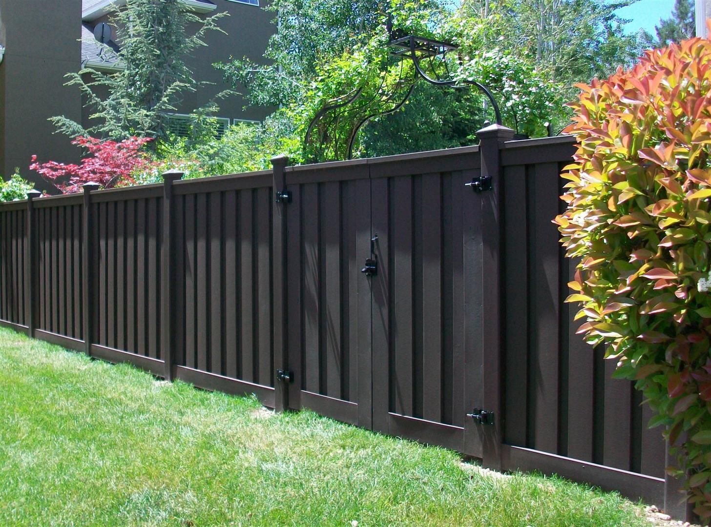 Brown wooden fence with gate in front yard with green grass and foliage.