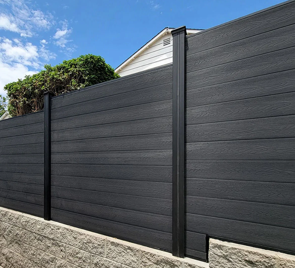 Black horizontal plank fence with black posts, against a blue sky, atop a gray stone wall.