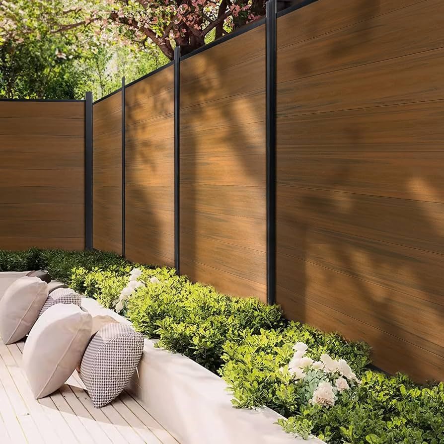 Wood-look fence with black posts, bordering a patio with pillows and green shrubbery.