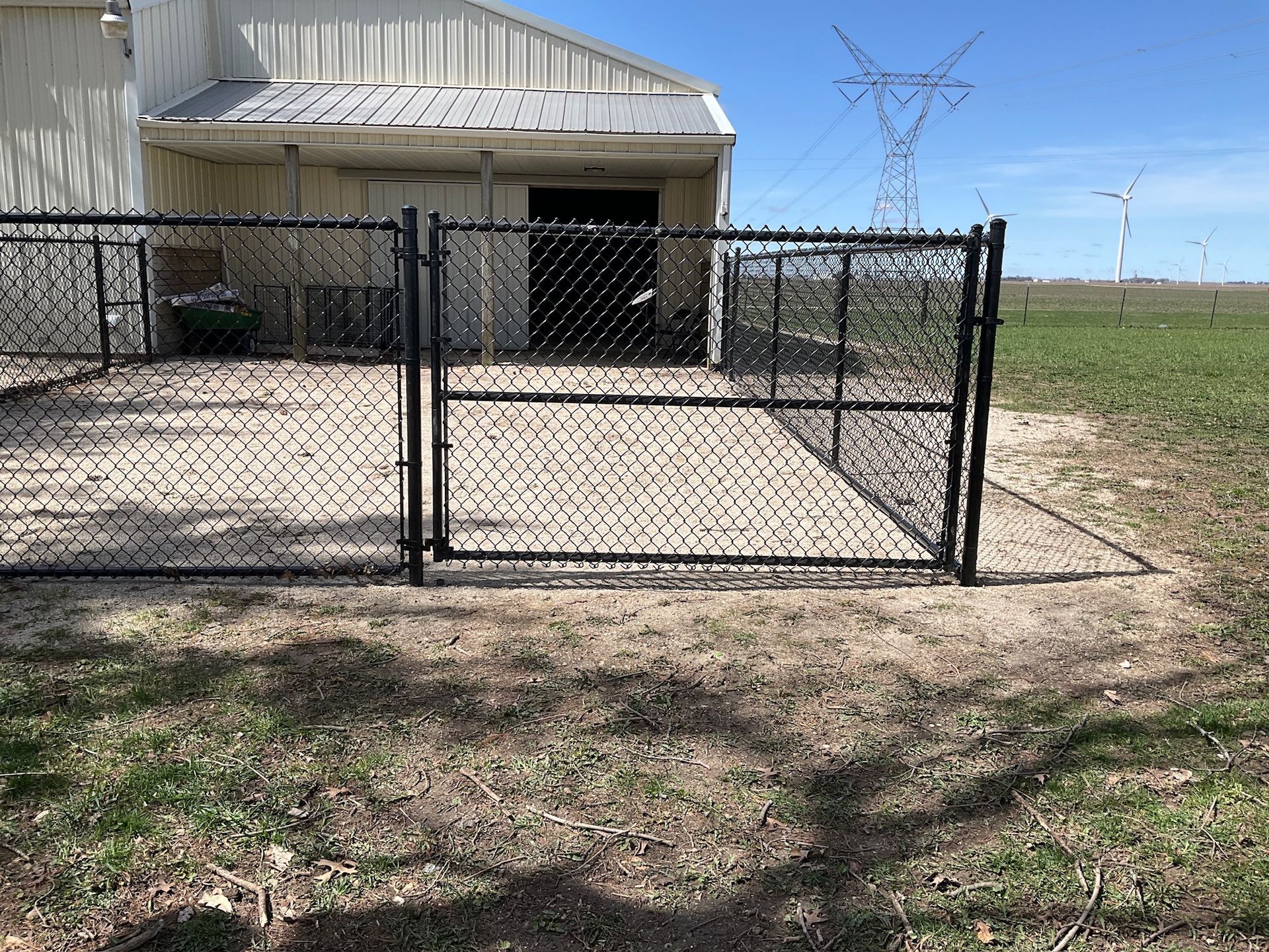 Black chain-link fence with gate in front of a tan building. Green grass and blue sky.