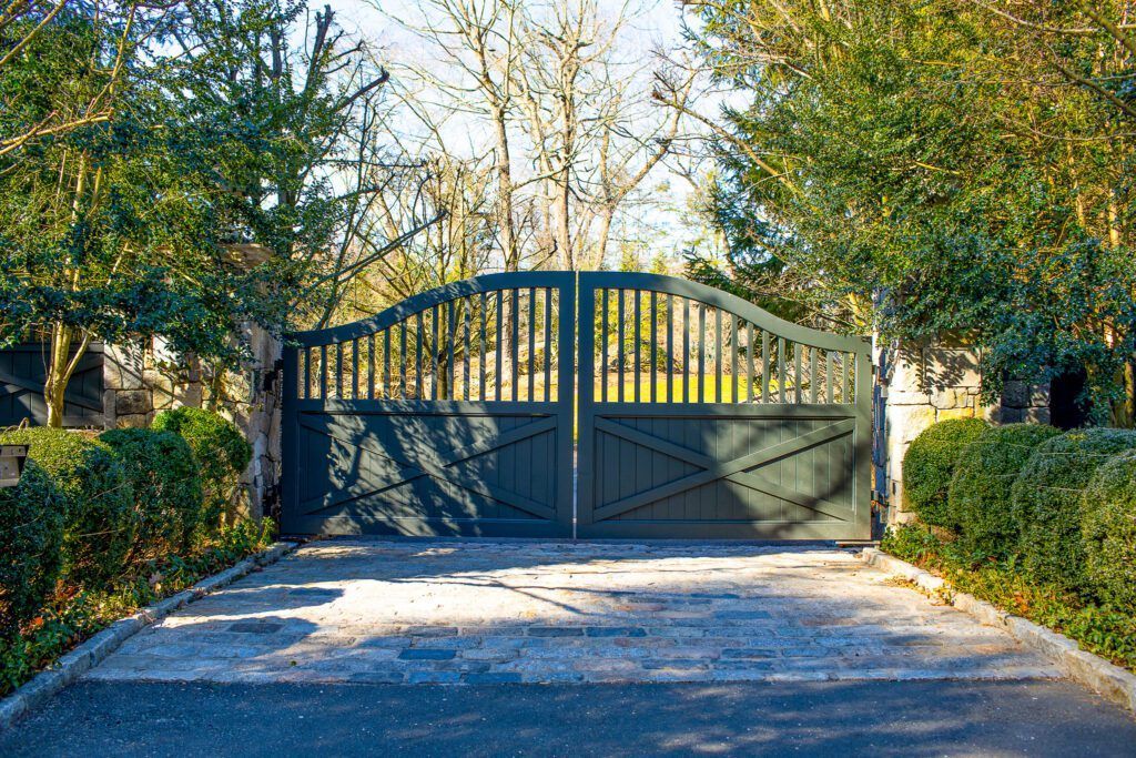 Dark green gated entrance to a driveway flanked by green bushes and trees.
