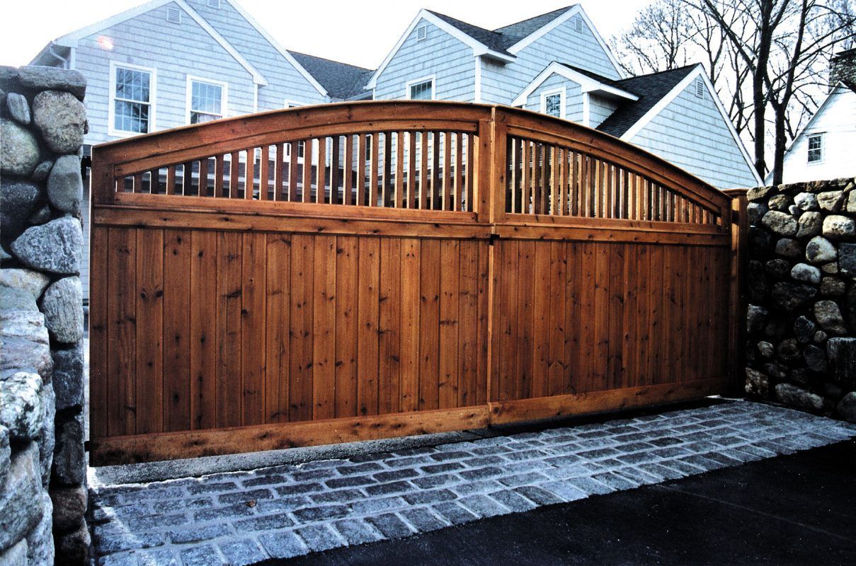 Wooden gate between stone pillars, arched top, set in brick driveway.