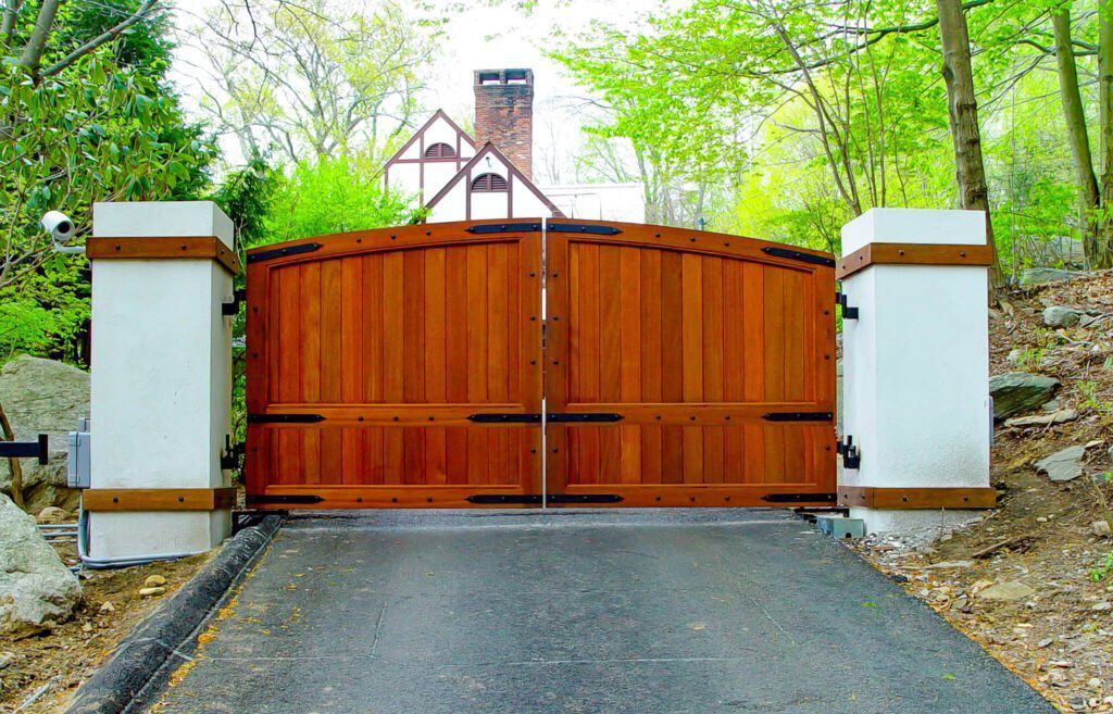 Wooden gate with white pillars and asphalt driveway leading to a house.