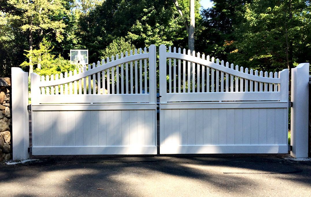White wooden driveway gates, arched top with vertical slats, set between stone pillars.