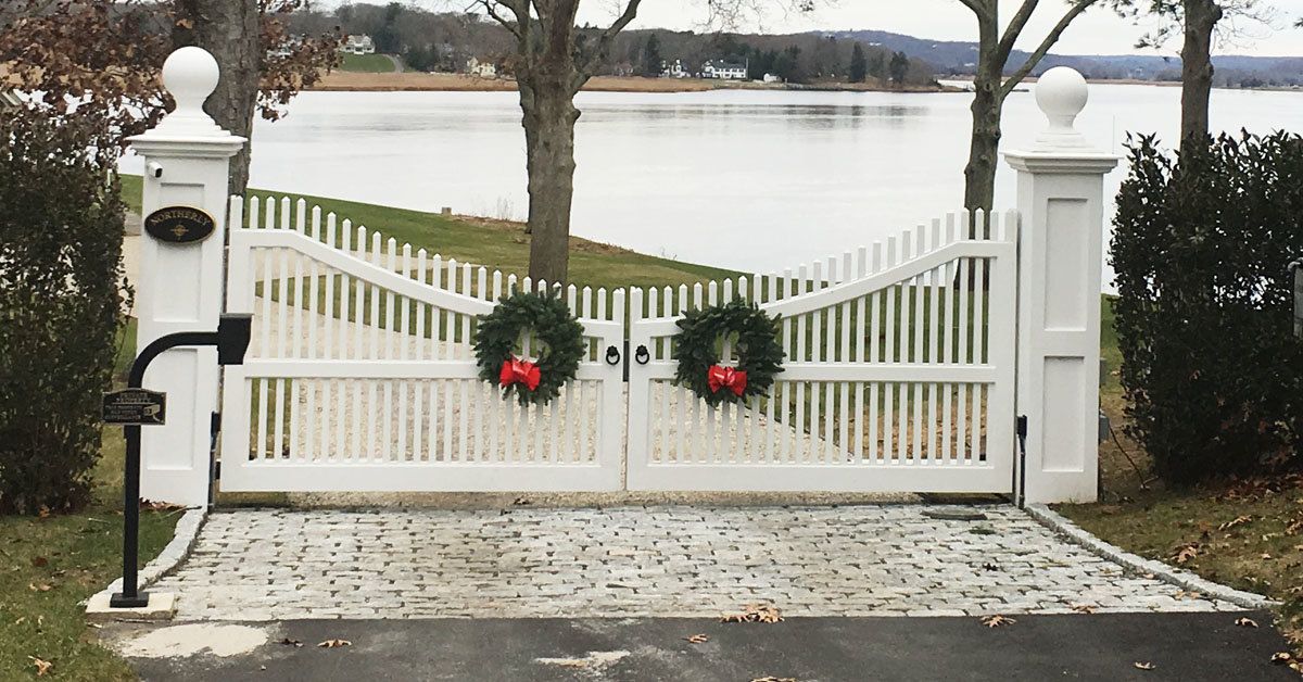 White picket gate with wreaths, leading to a lake.