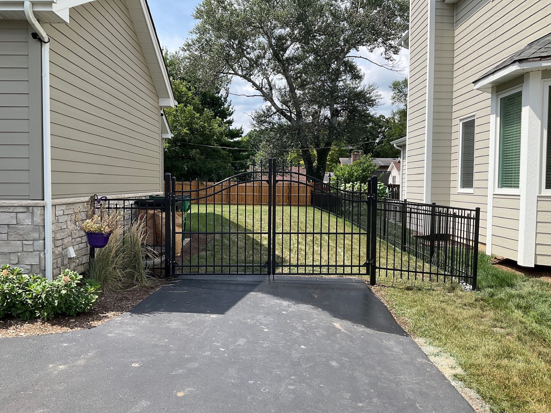 Black metal gate and fence in front of a backyard, between two houses, on asphalt.