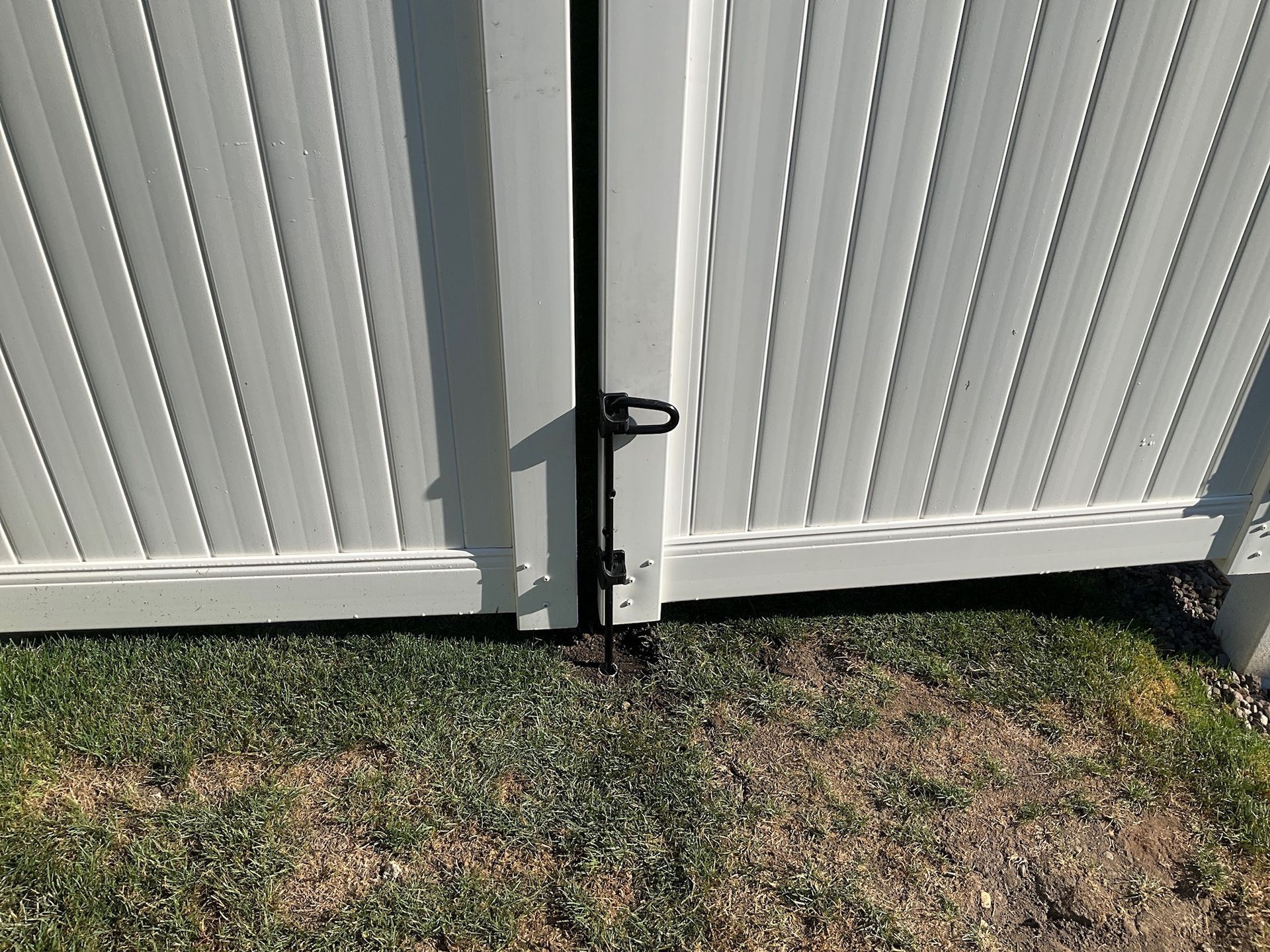 White vinyl fence gate with a black bolt latch, set in a grassy yard.