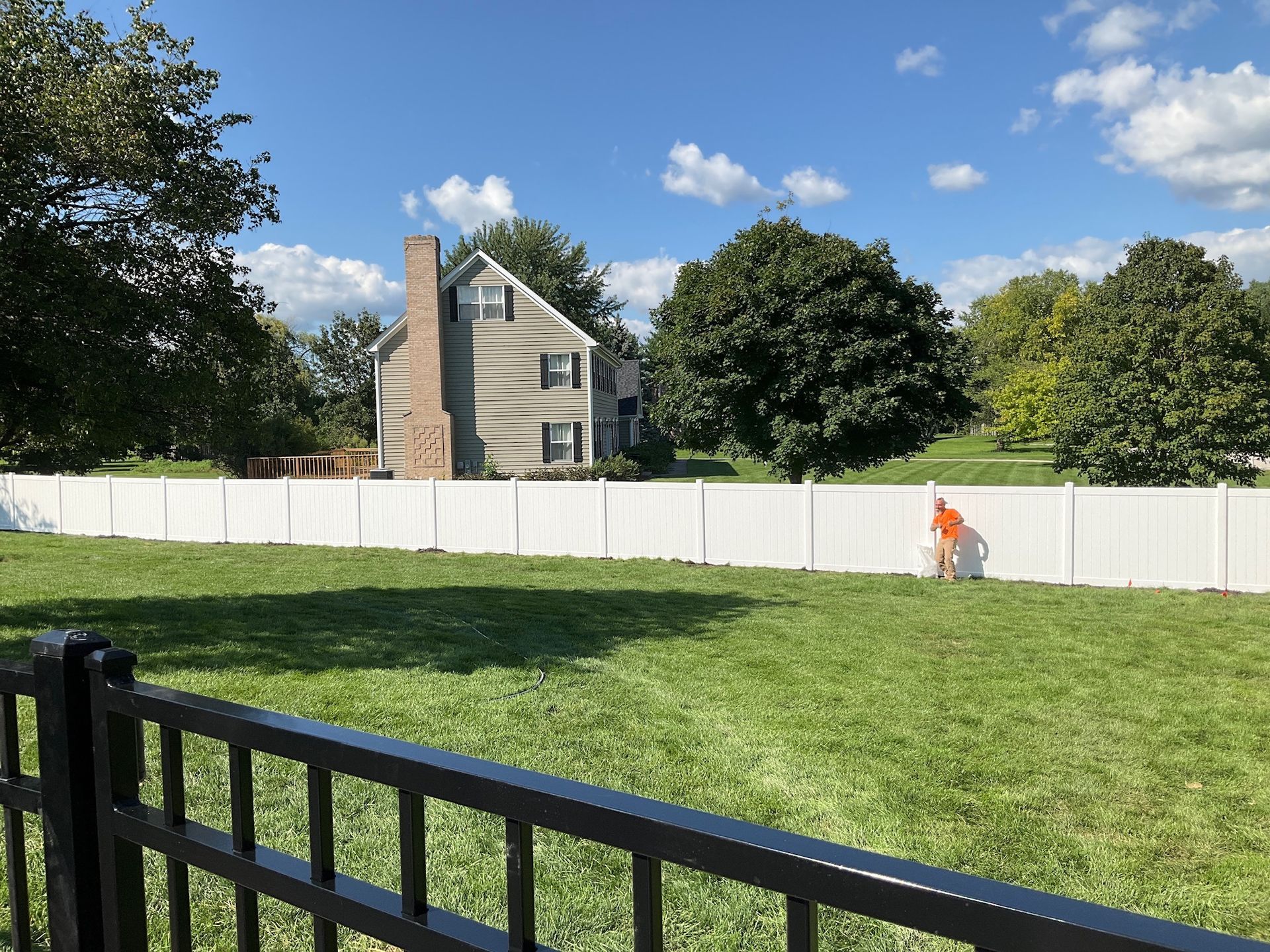 House behind a white fence on a grassy lawn under a blue sky.