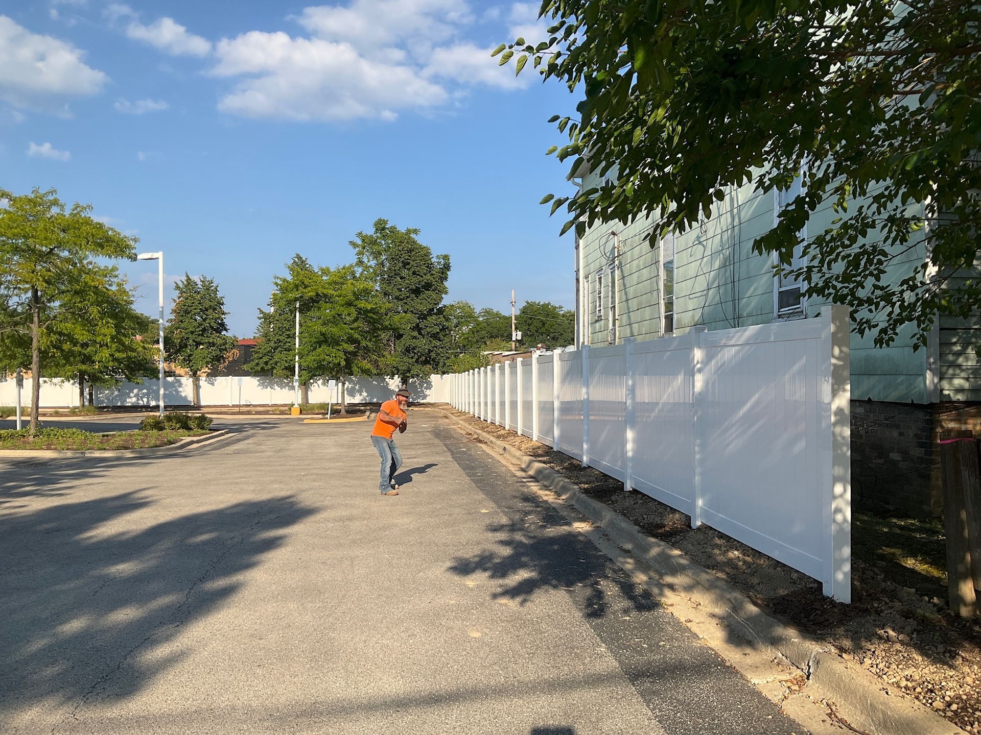 Person throwing something in a gravel lot next to a white fence. Sunny day.