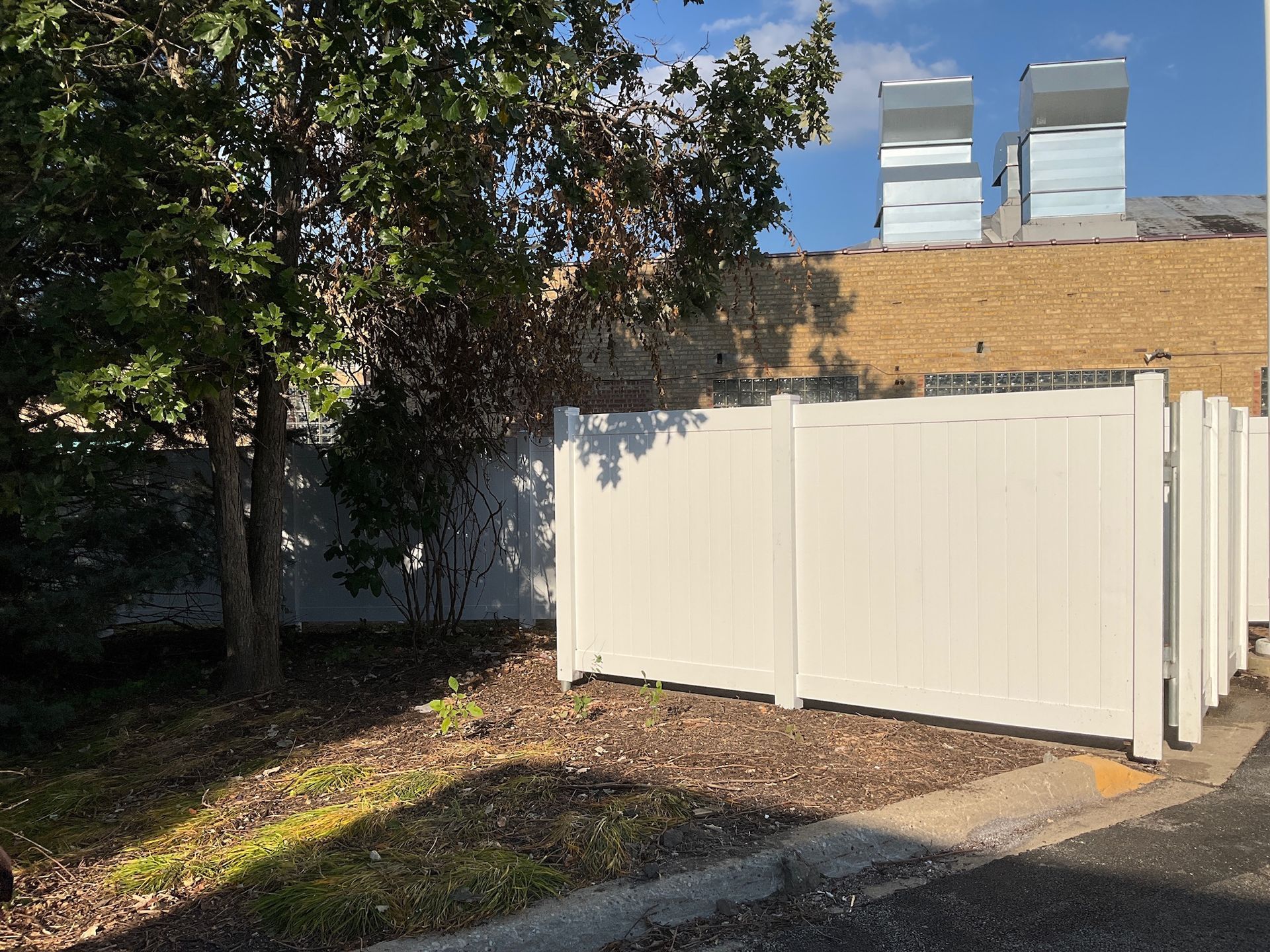 White fence near trees and building rooftop with silver vents.