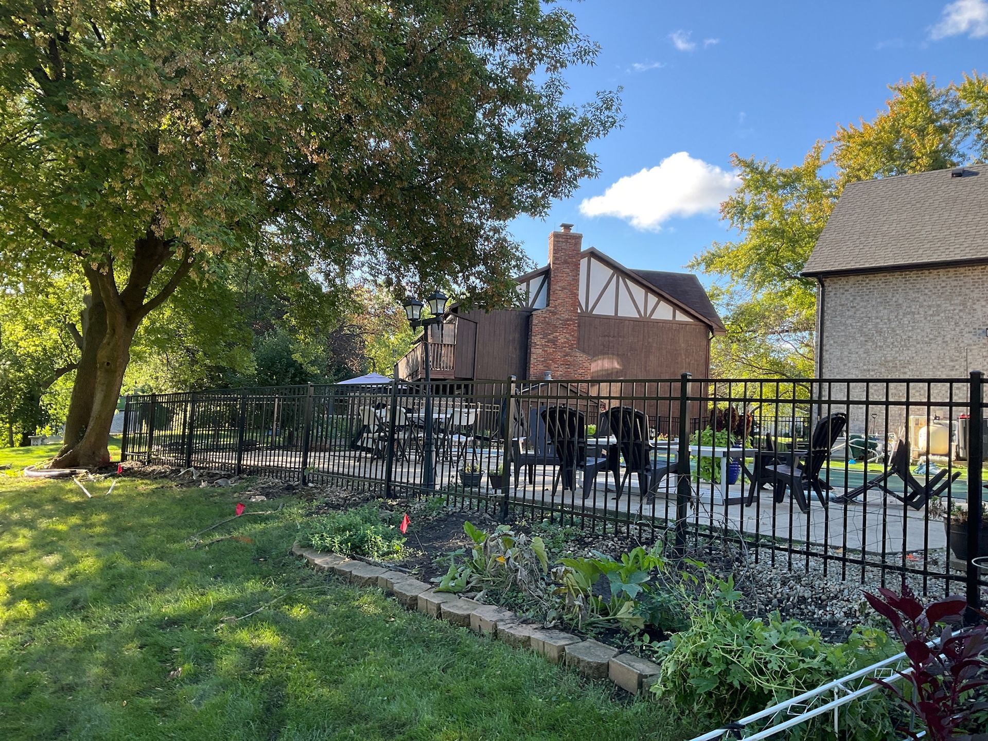 Backyard scene with black metal fence, patio furniture, and two-story house with brick and brown siding.