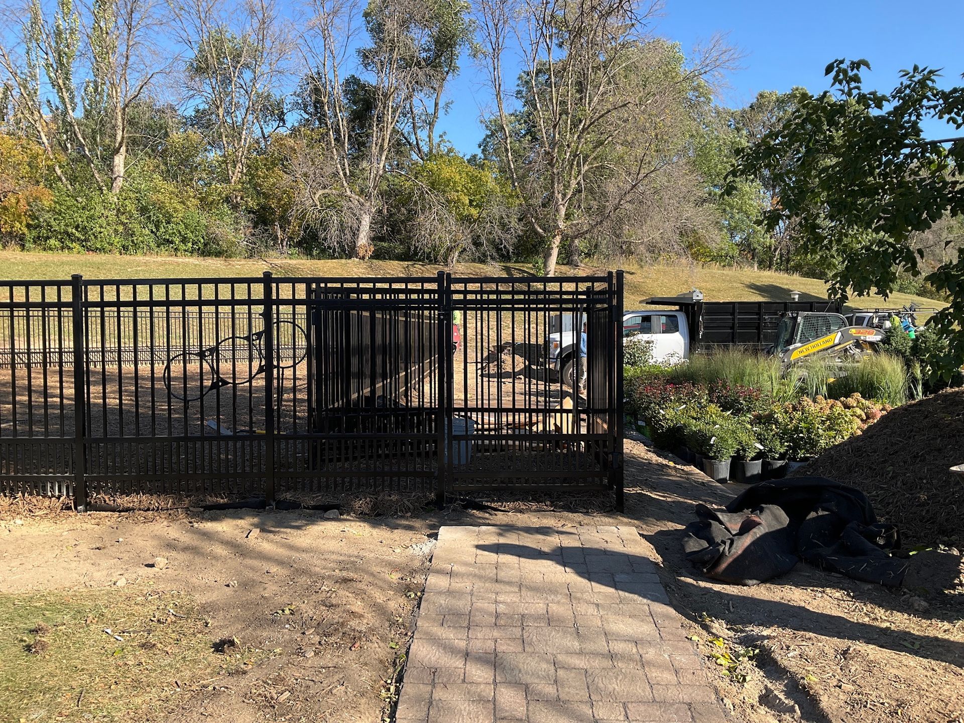Black fence enclosing an area with plants, brick pathway, and vehicles.