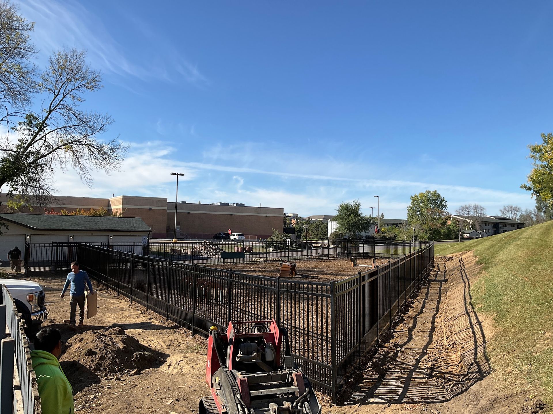 Construction site with black metal fence being installed on a dirt lot. Blue sky.