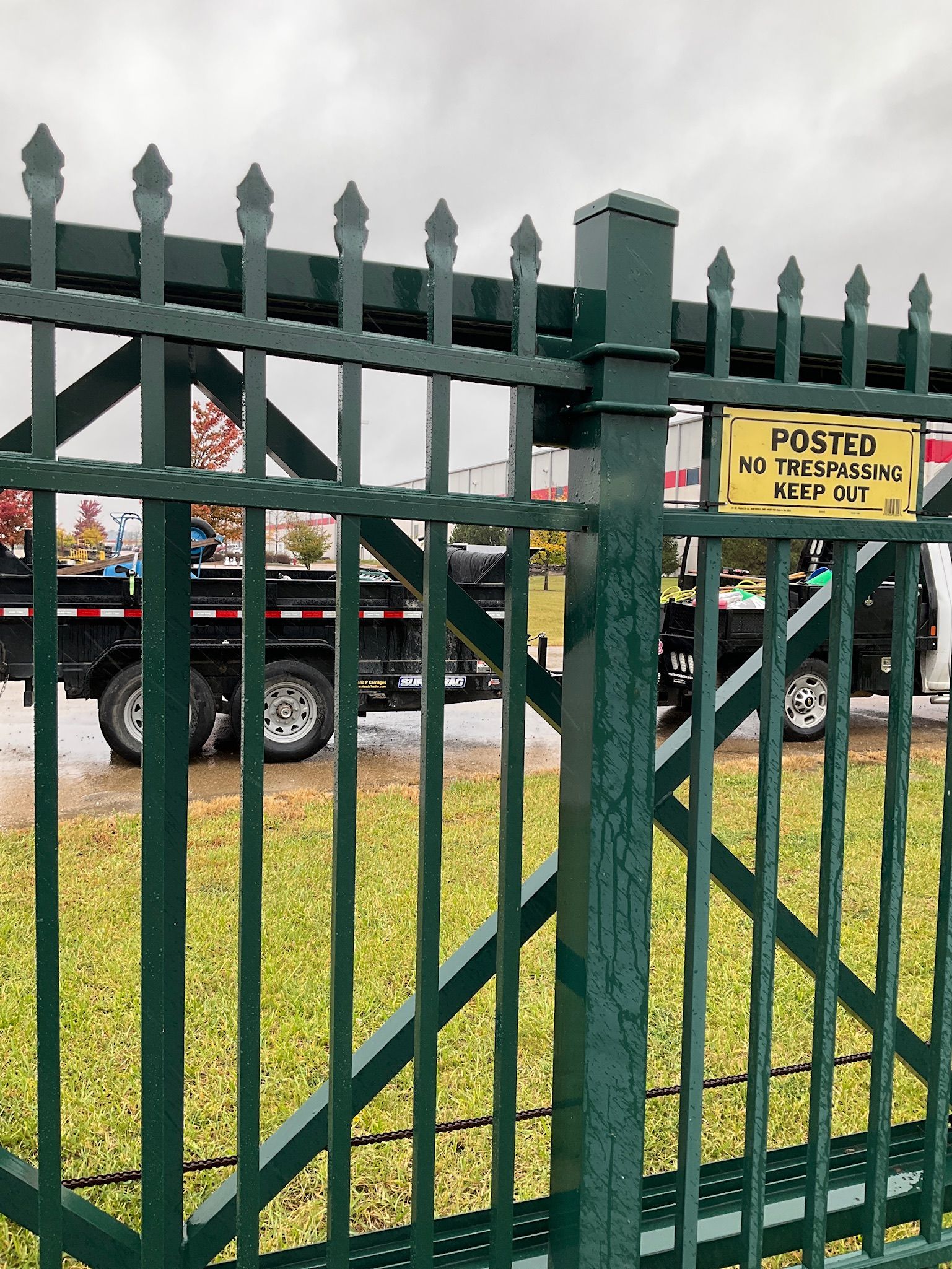 Green metal fence with a sign, truck in the background. Overcast day.