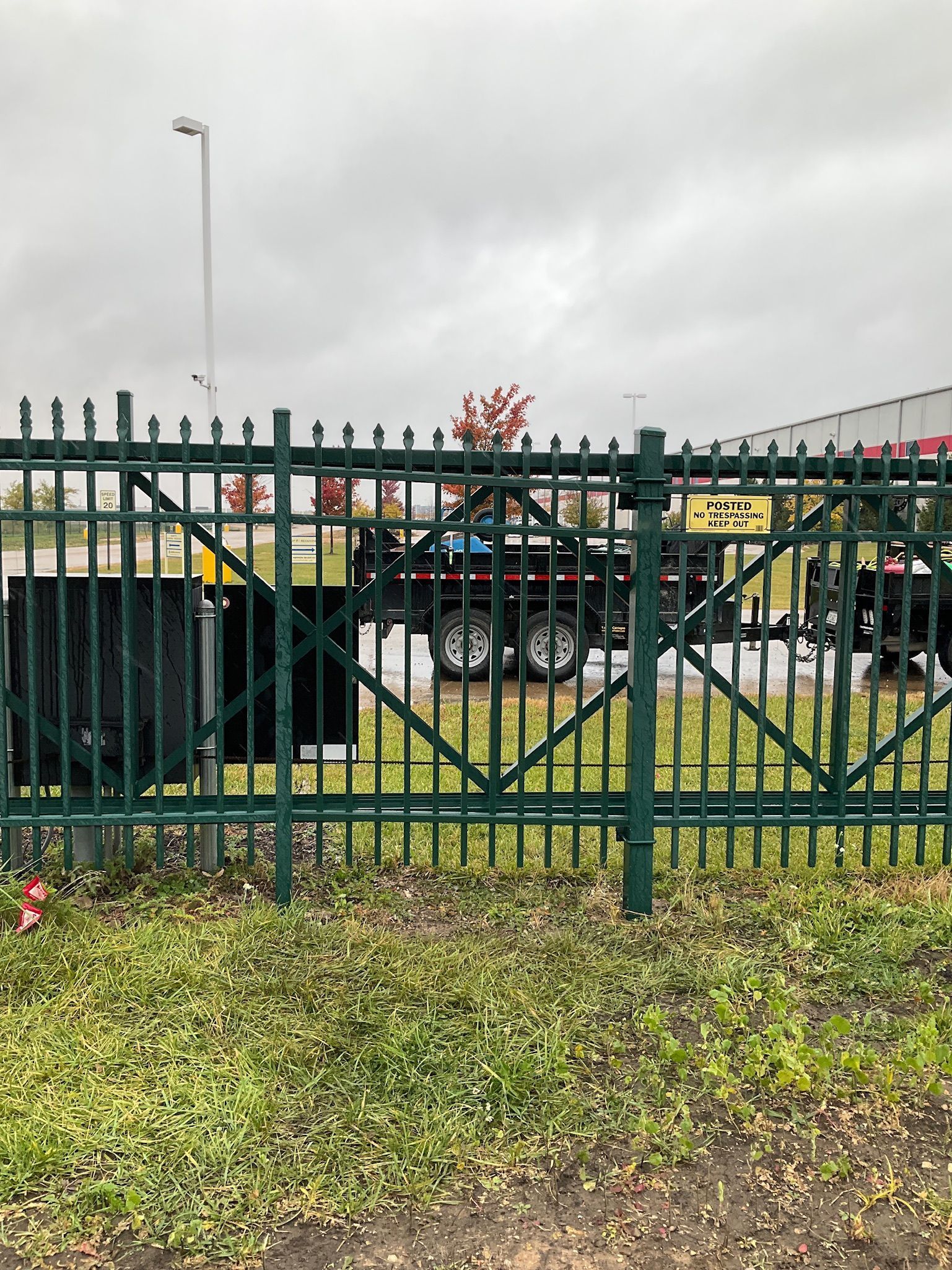 Green metal gate with trailer and grassy foreground on a cloudy day.