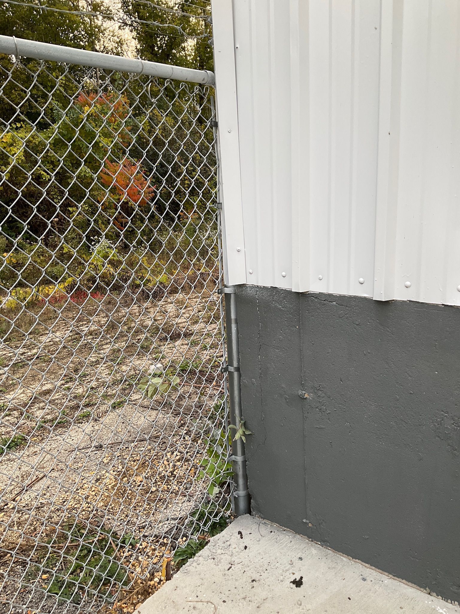 Chain-link fence next to a building with a gray lower portion and white upper portion, on a concrete slab.