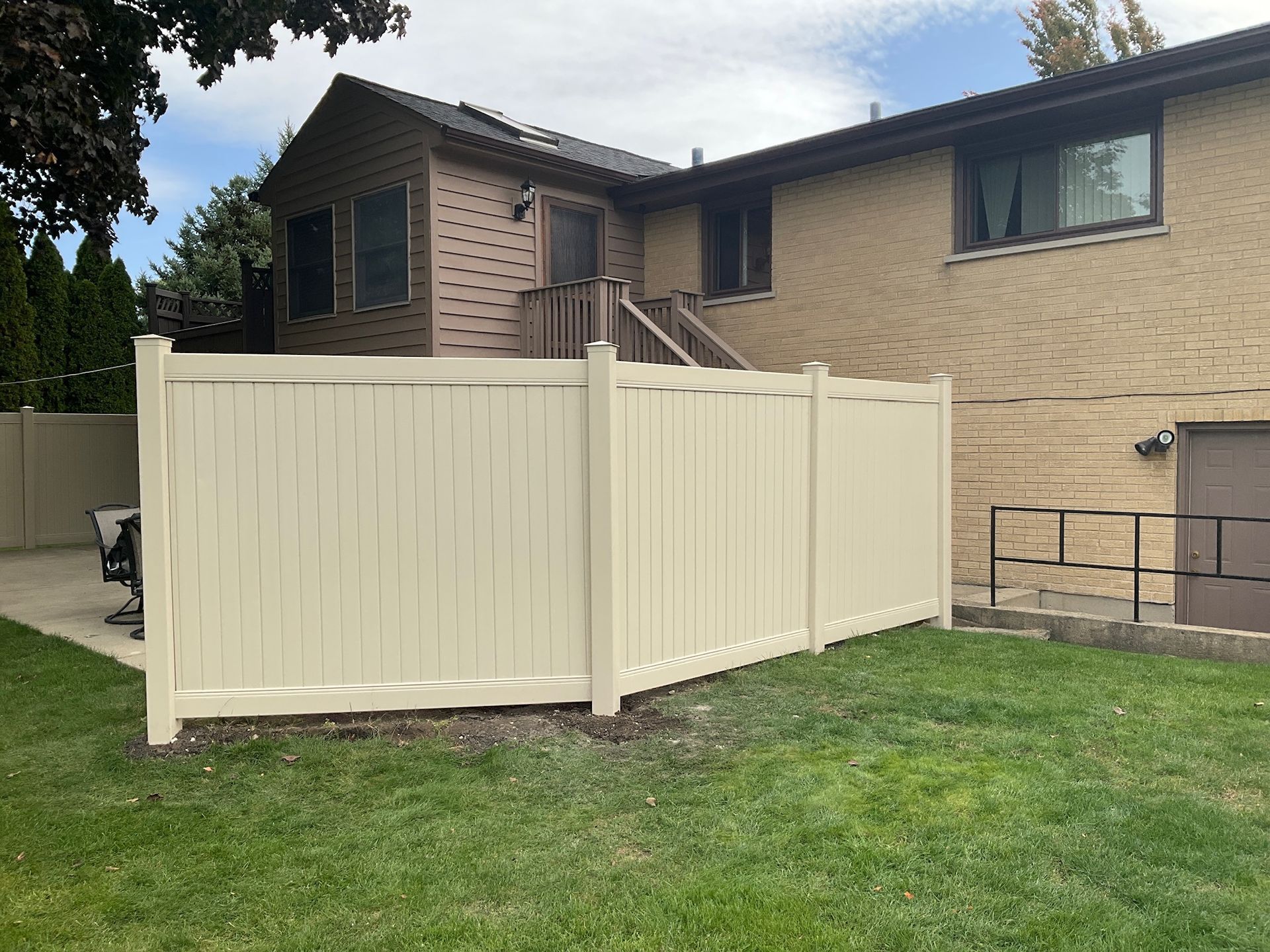 Beige vinyl fence enclosing a green lawn in front of a tan brick house.