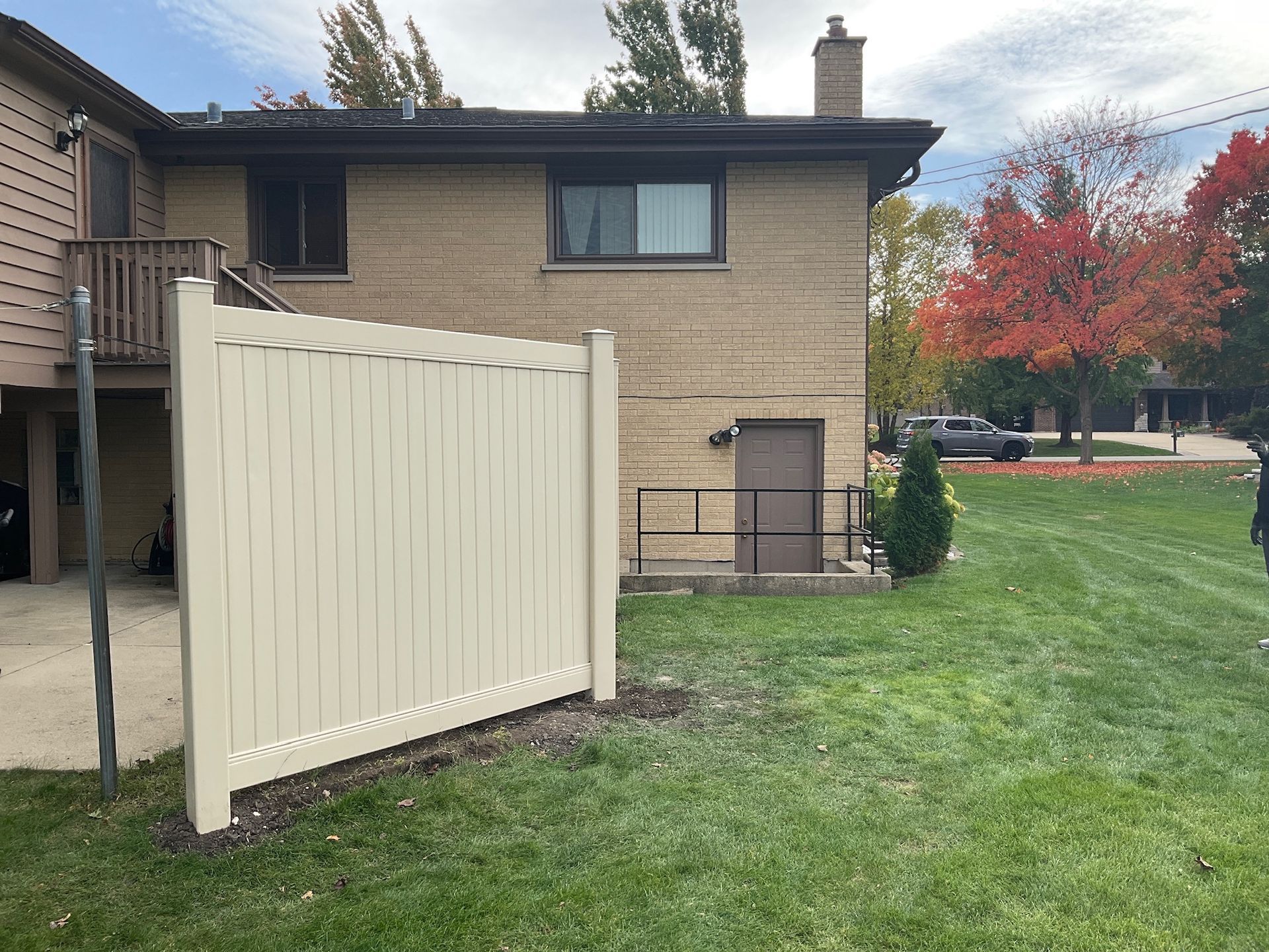 Beige vinyl fence next to a brick building with a brown door and a grassy lawn.