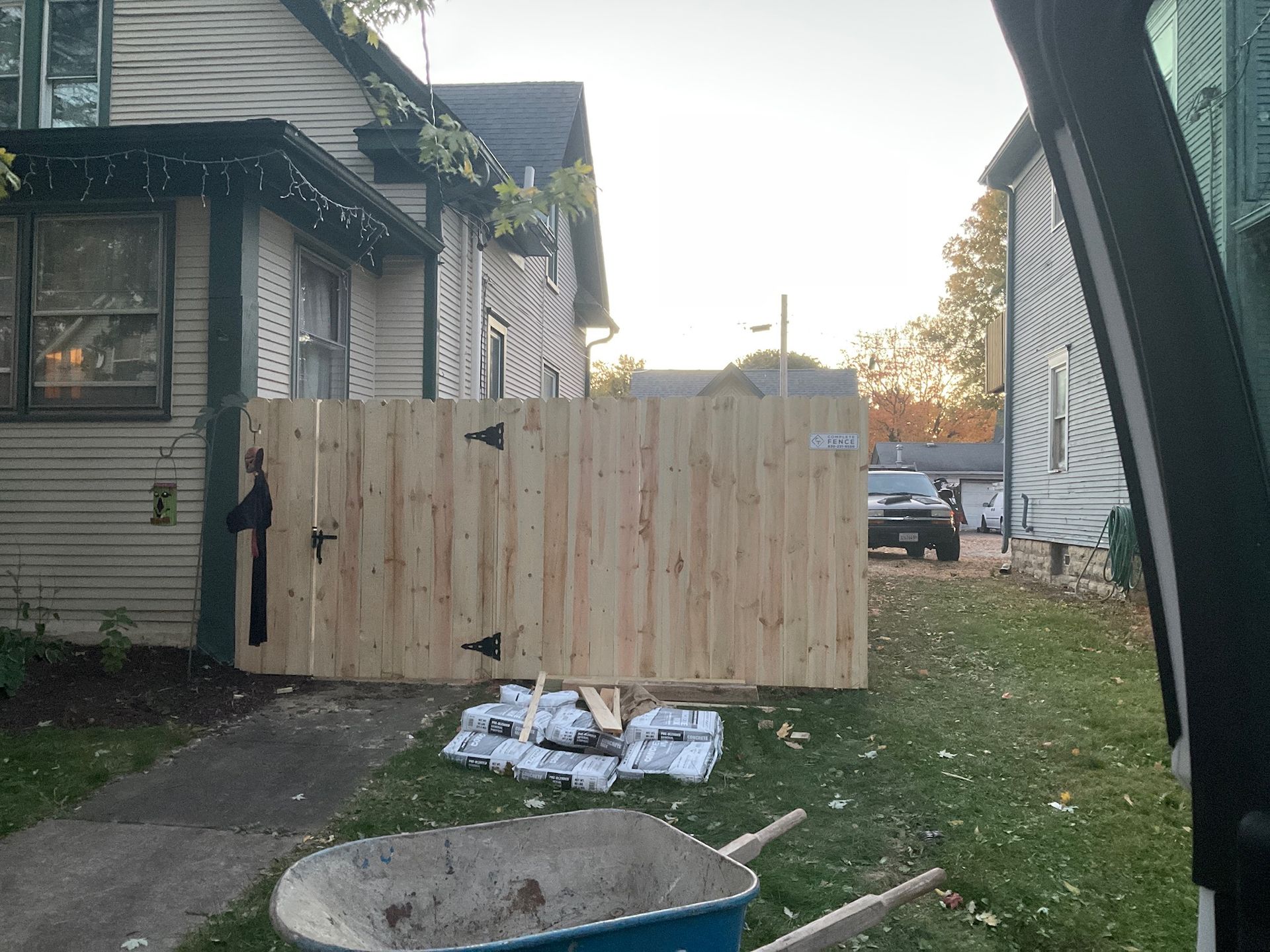Wooden fence installed between two houses, with construction supplies and a wheelbarrow in front.