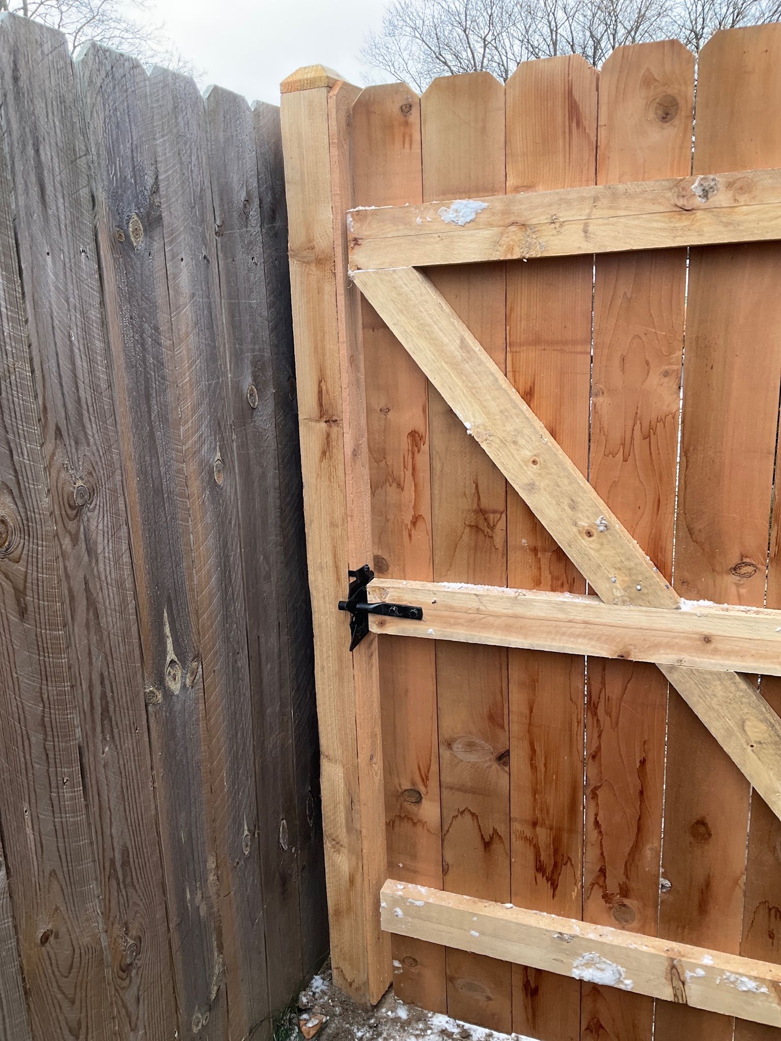 Wooden fence with a gate. Gate is open, showing a black latch.