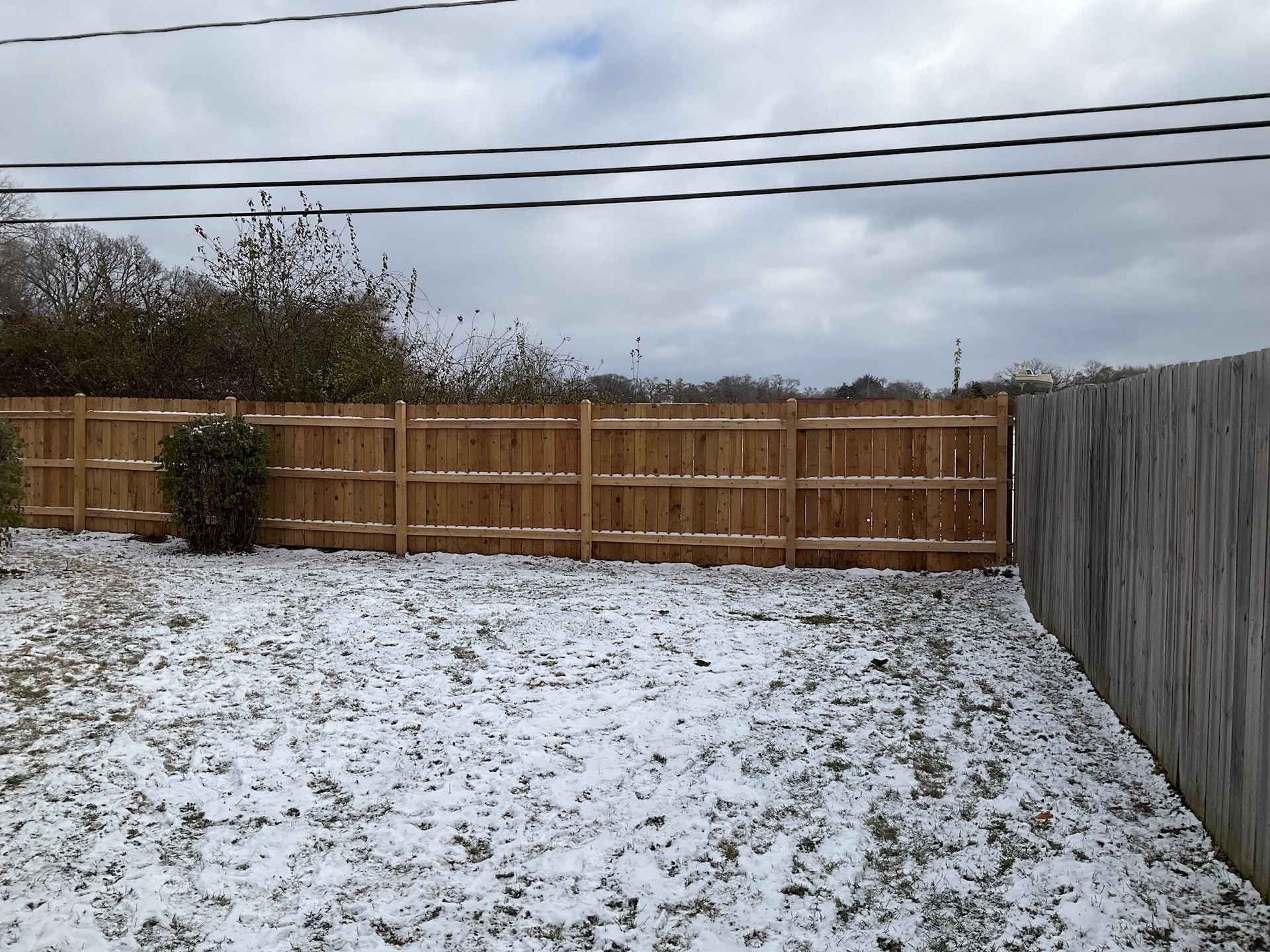 Snowy backyard with wooden fences under a cloudy sky.