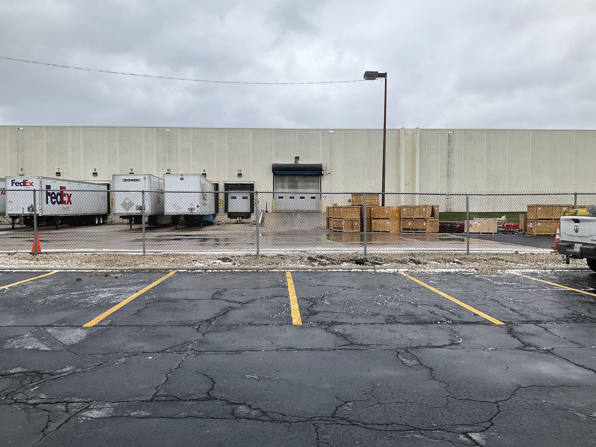 Exterior of a FedEx facility on a cloudy day. Trailers, loading dock, pallets, and parking lot visible.
