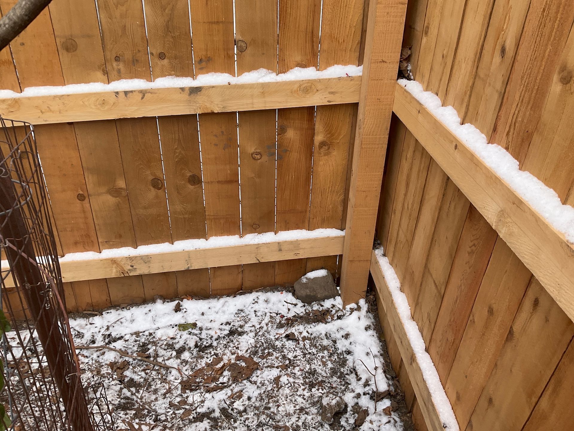 Wooden fence corner, with snow along the top and on the ground.
