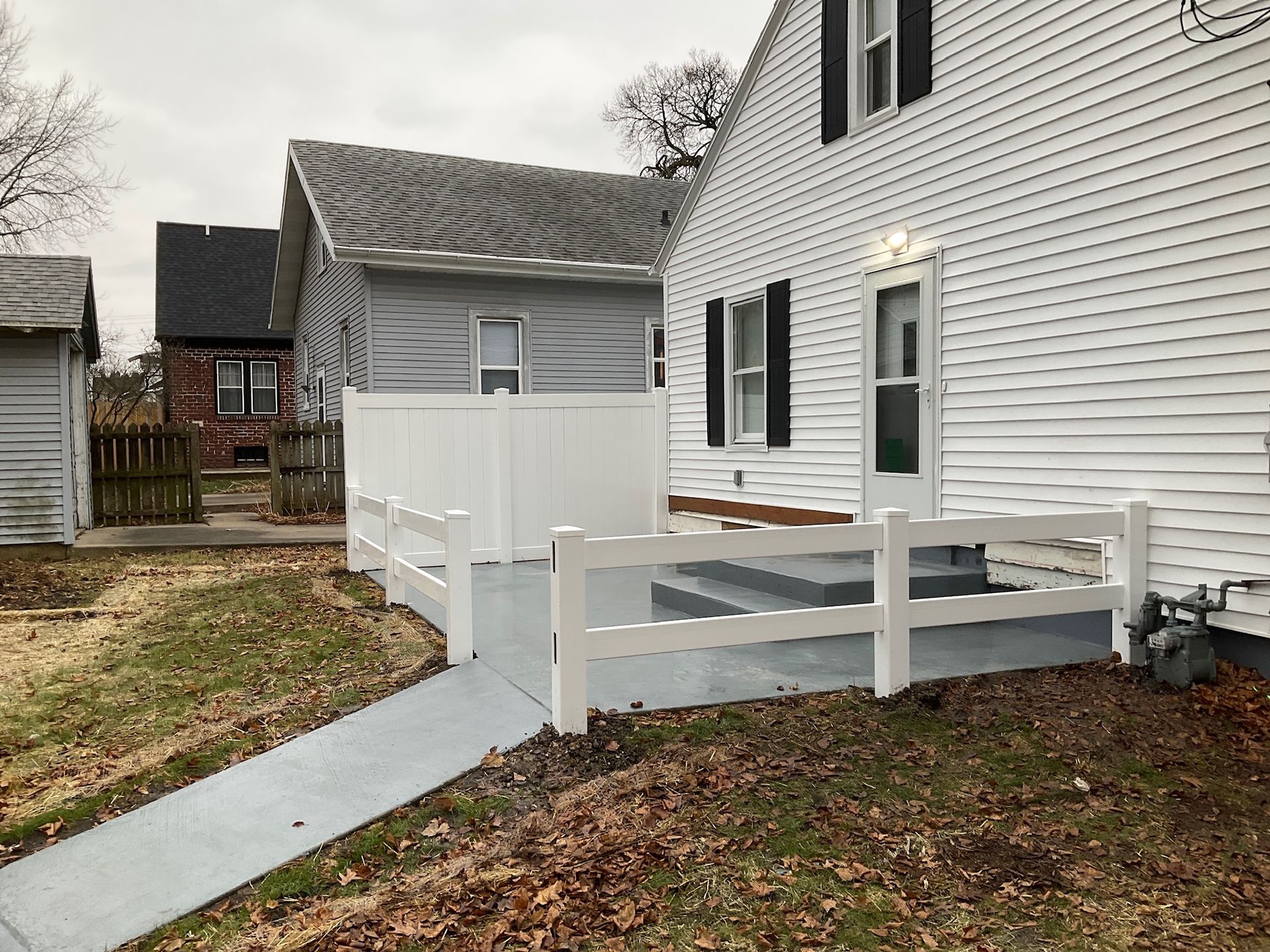 White house with a new white fence, gray walkway. Cloudy day.