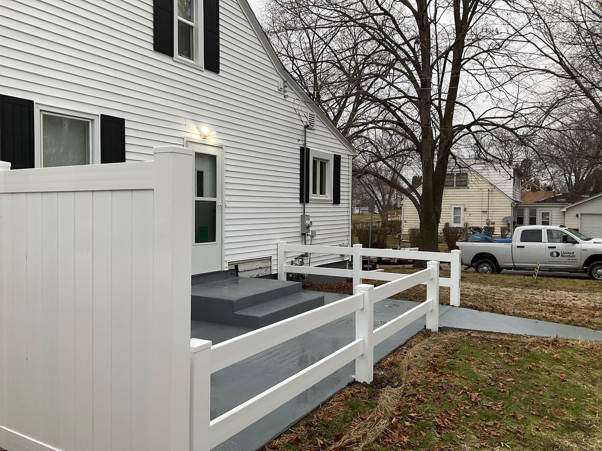 White house with white fence and steps, a truck in the distance.