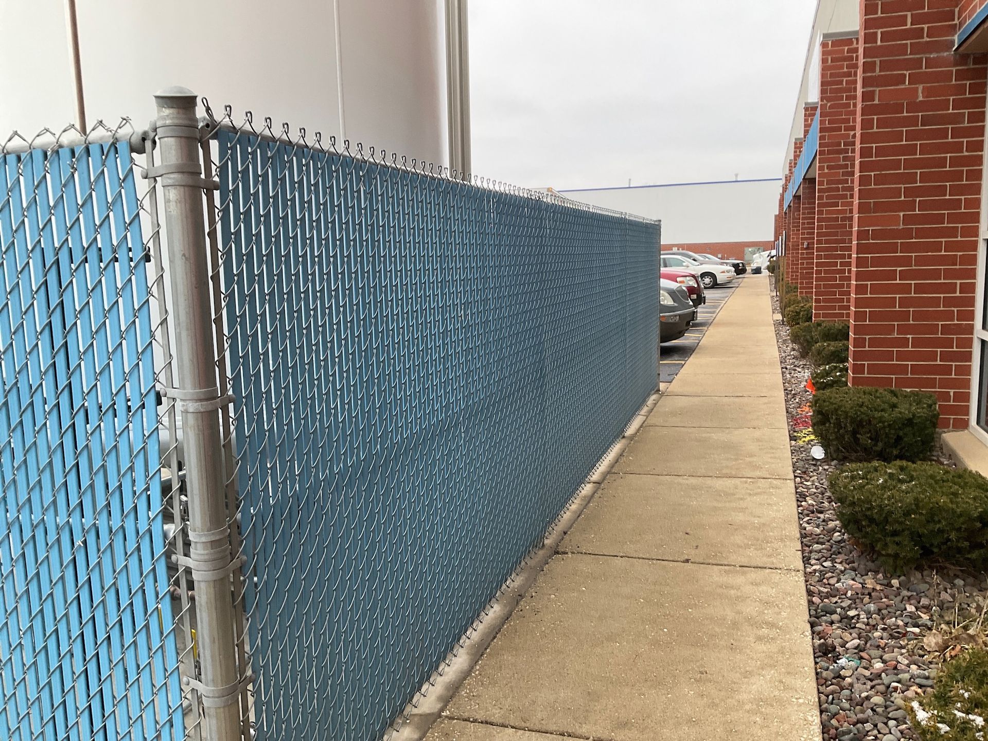 Blue privacy fence along a sidewalk next to a brick building.