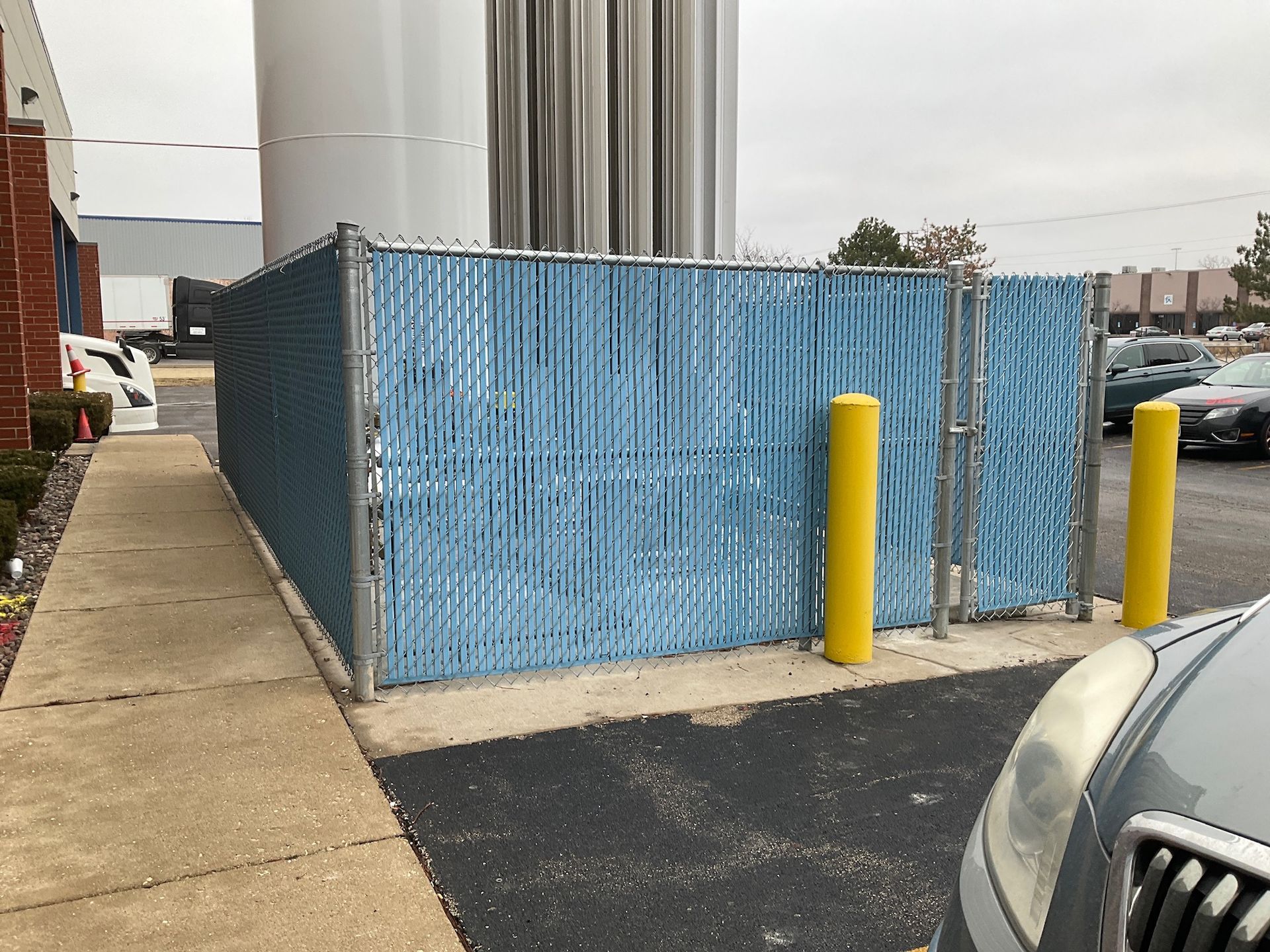 Blue privacy screen on a chain-link fence, next to a building and parked cars.